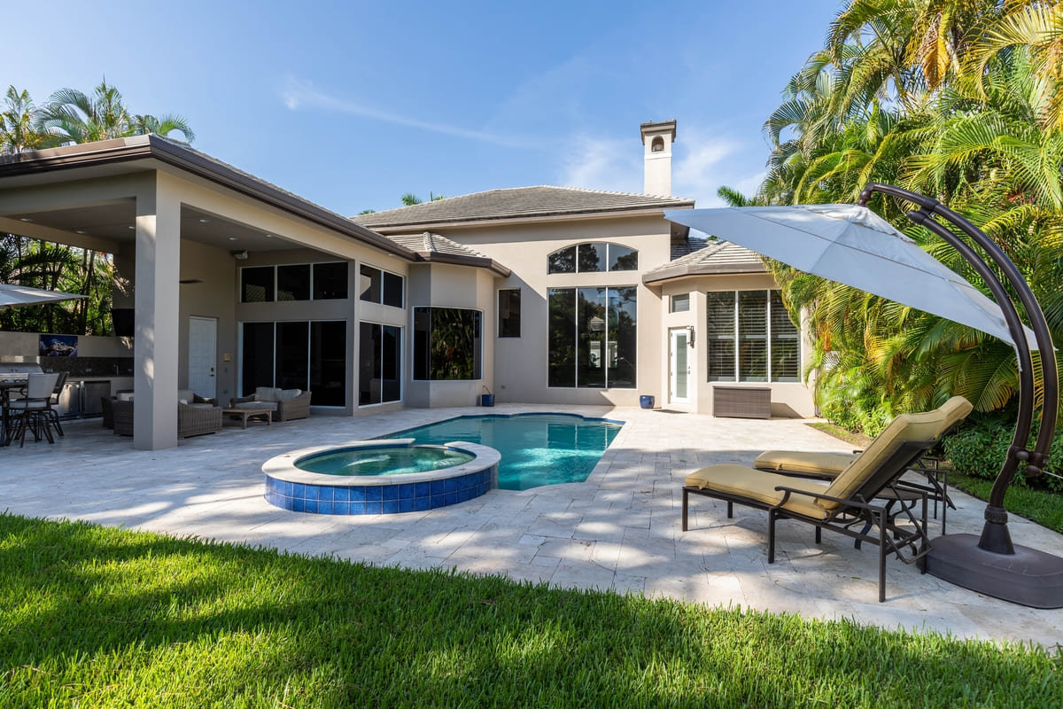 A small Floridian in-ground pool behind a white home.