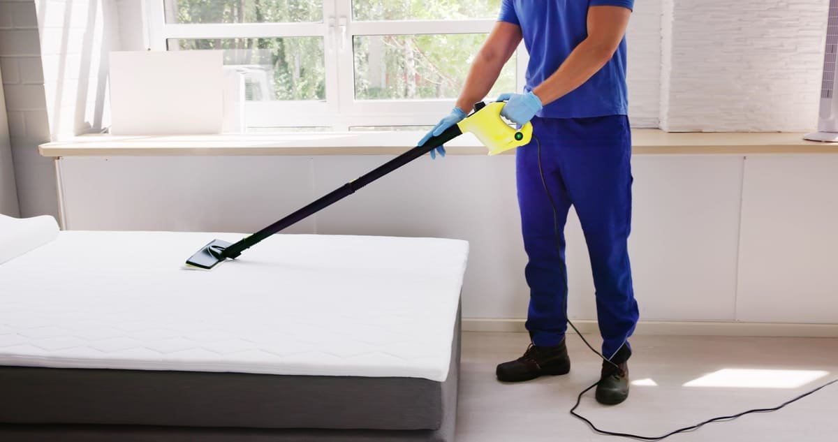 A person steaming a bed to remove an infestation of bugs.