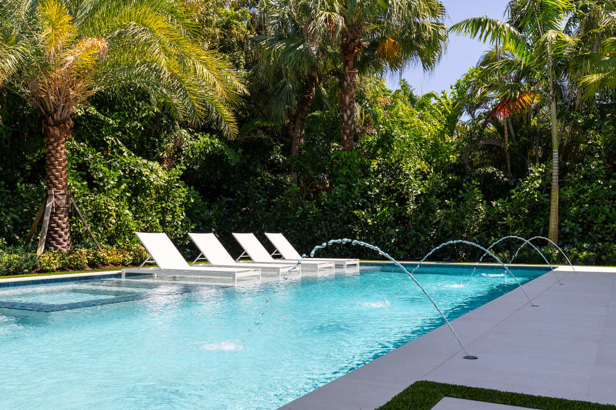 4 white sunbathing chair sitting next to a beautiful Florida pool.